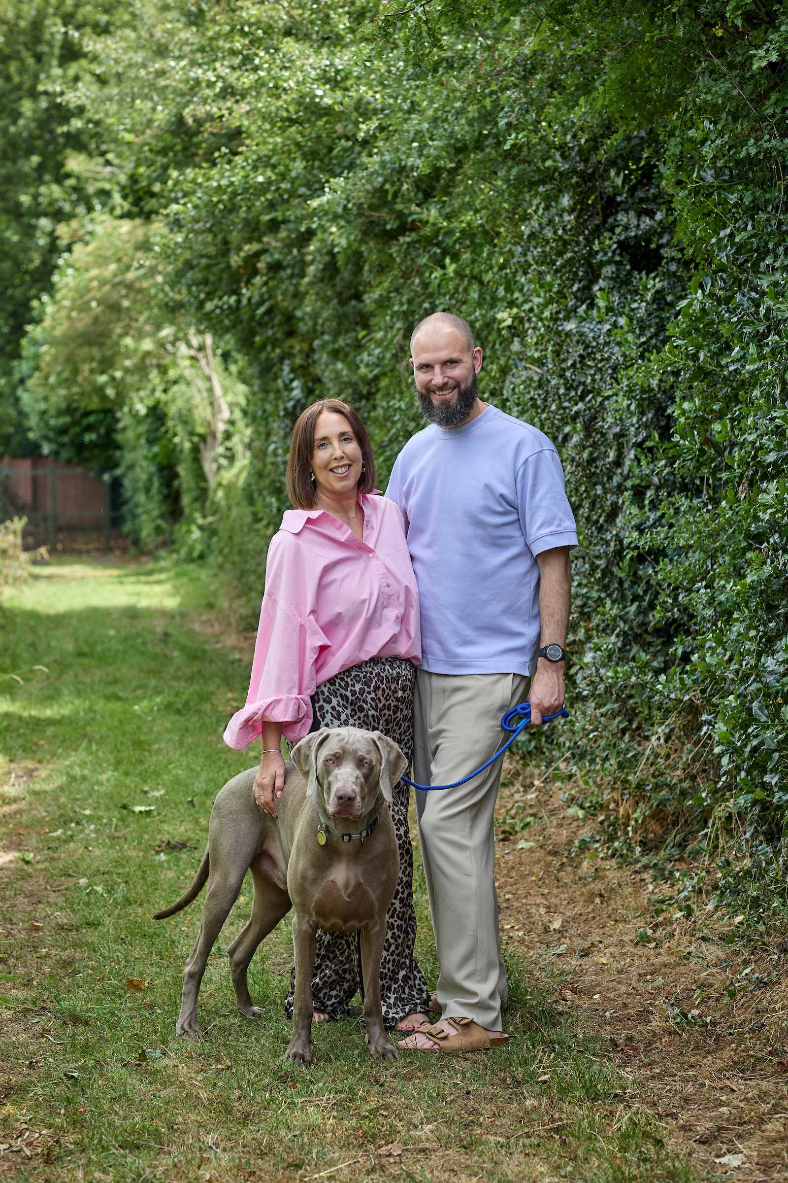 250629_icr_sally_steadman-south_0619 Sally and her husband stand in their garden with their dog, a grey Weimaraner