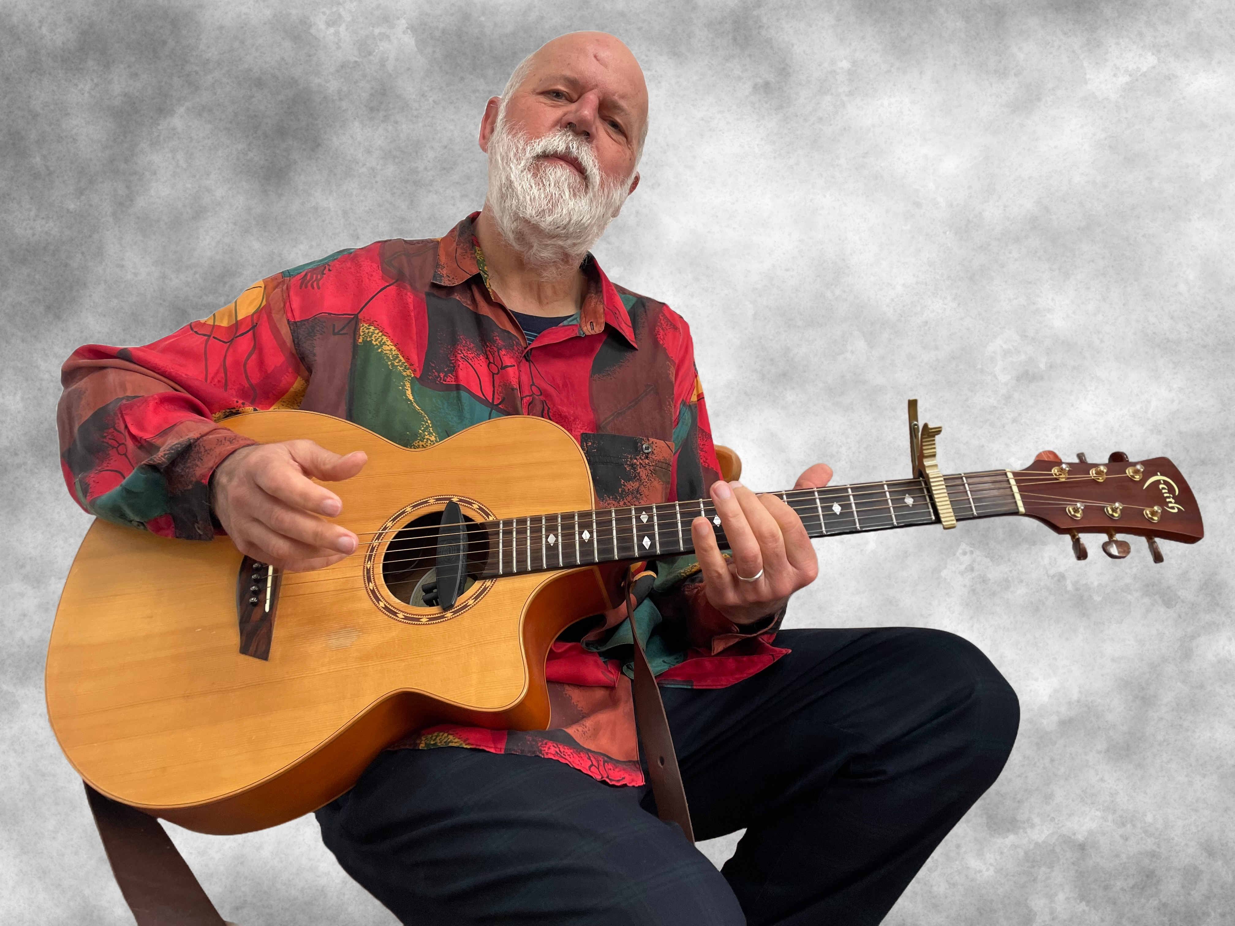 Credit Peter Laing Peter dressed in a bright red shirt holds a guitar and looks down at the camera