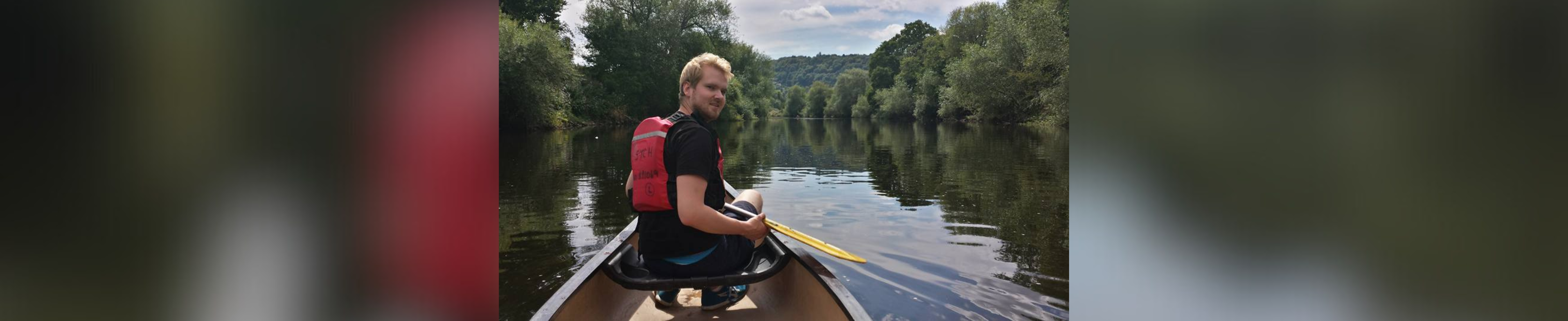 James Morden in a boat on the water with green shoreline in the background.