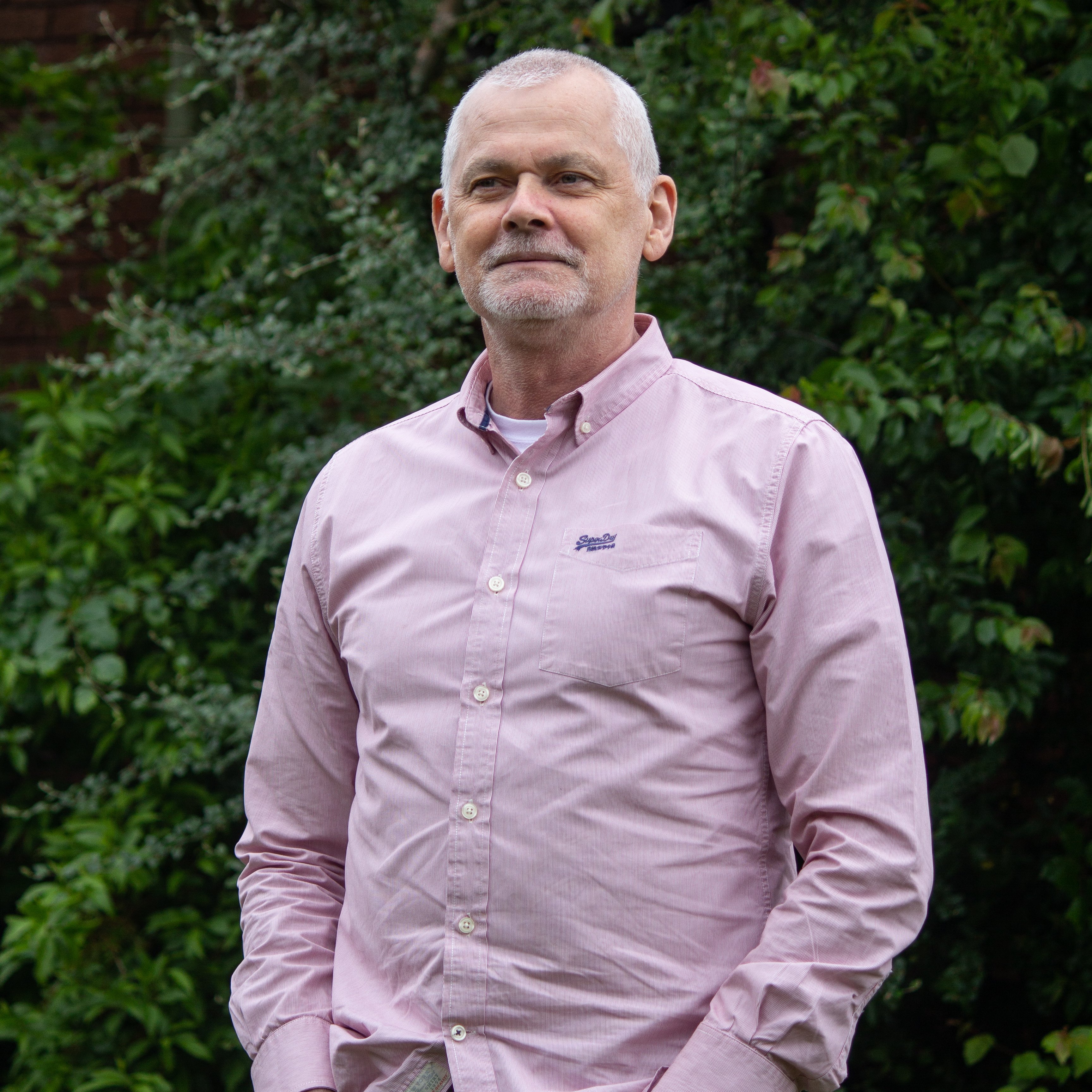Martin, a white man in his early 70s wearing a pink shirt looks into the distance