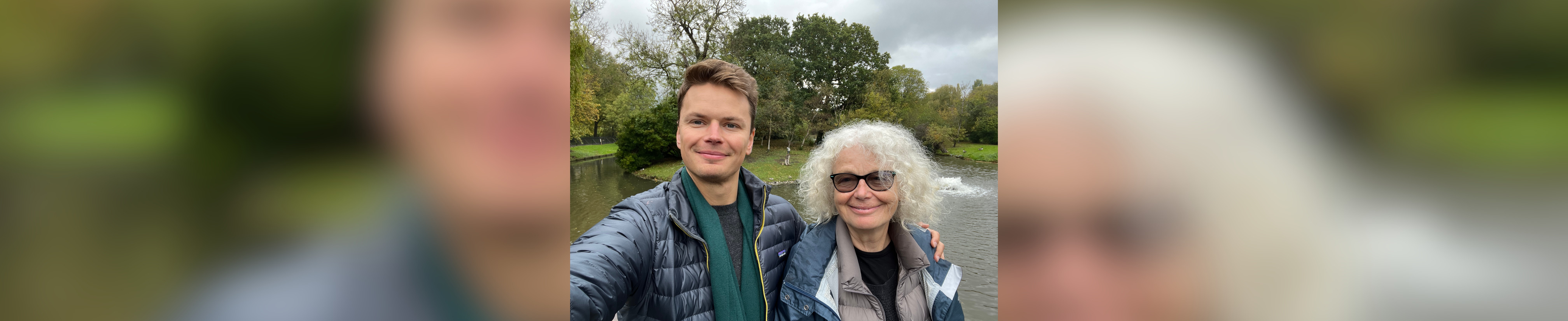 Oliver smiling with his Mum, they are standing in front of trees and a lake