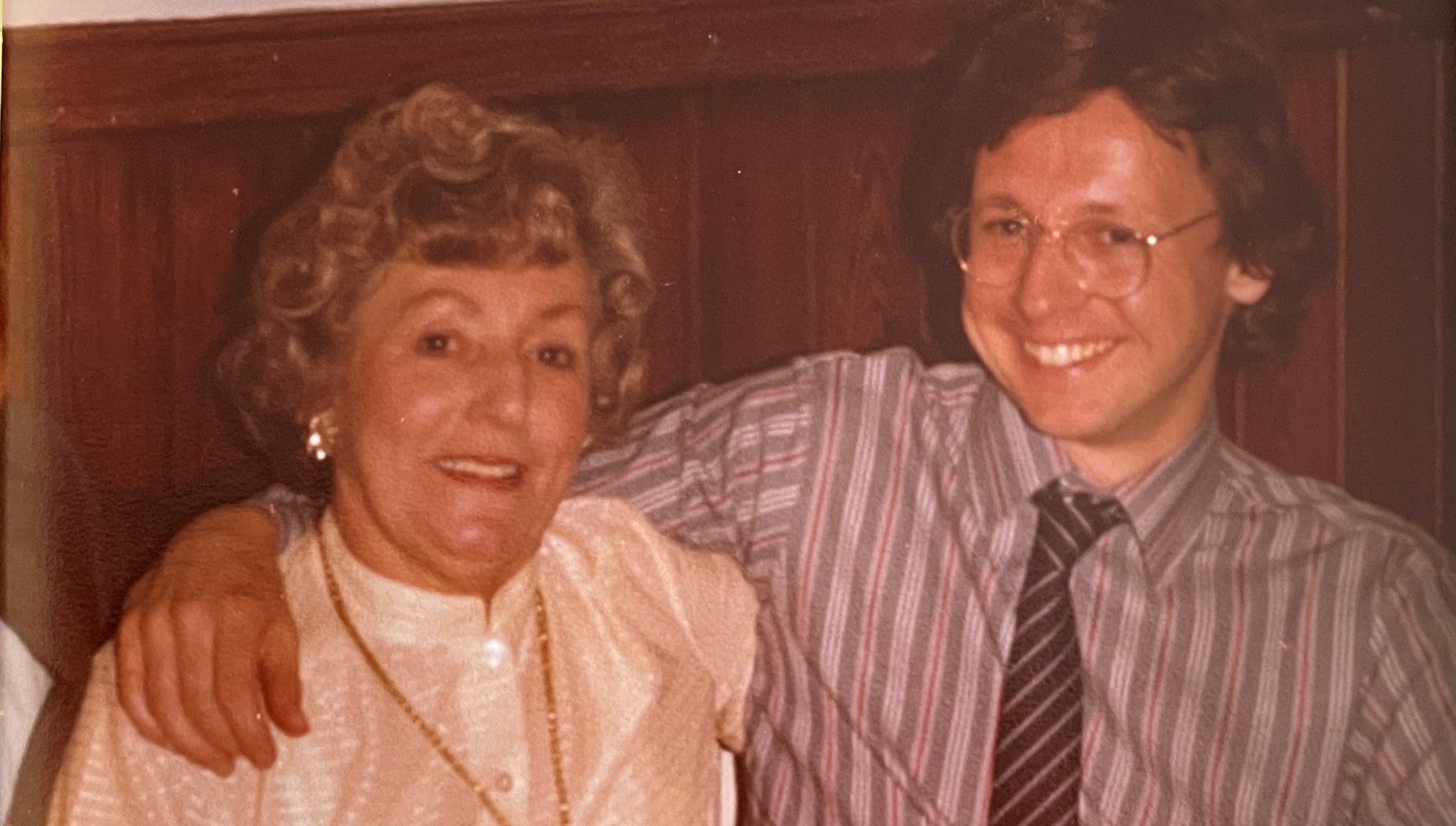 Paul with his mother in 1982. They're both smiling and he has his arm around her.