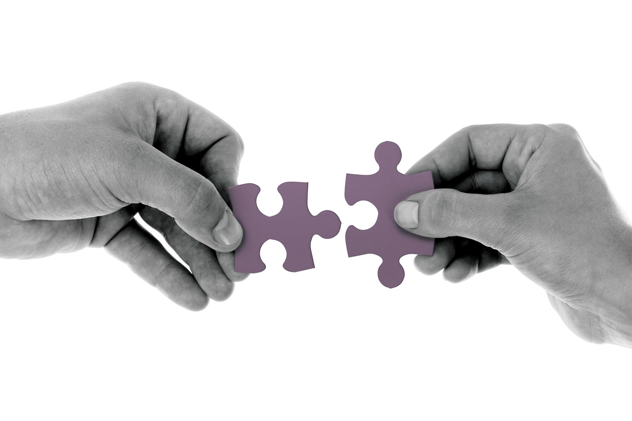 Two puzzle pieces fitting together Two hands, each holding a jigsaw piece and bringing the two together