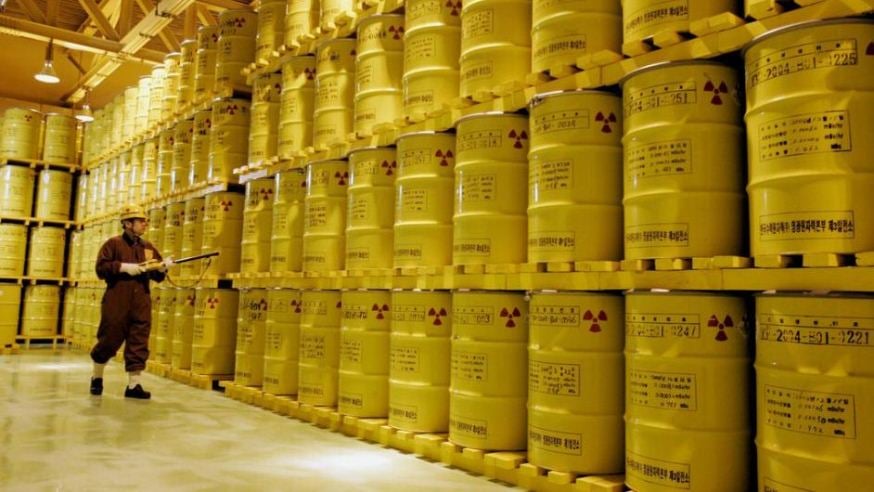 Waste adviser Waste adviser wearing protective uniform surveying barrels of radioactive waste