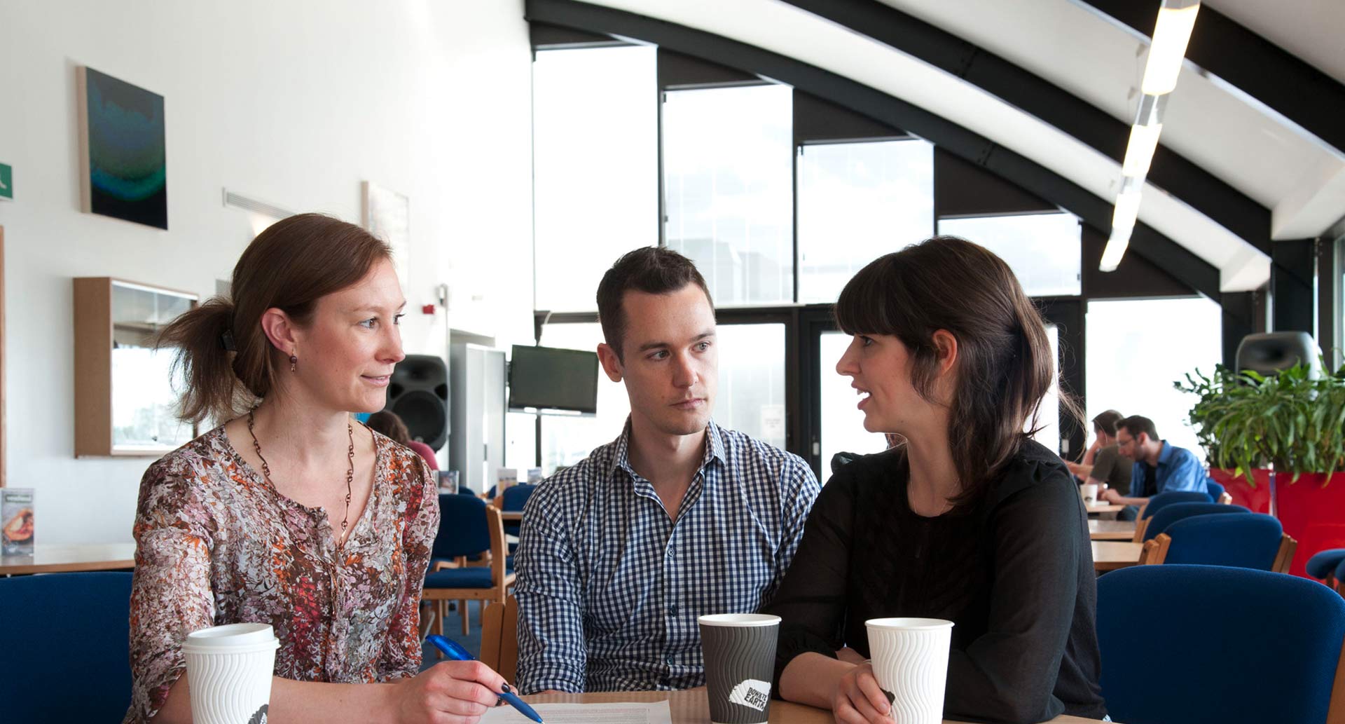 Three colleagues chatting having coffee in the canteen