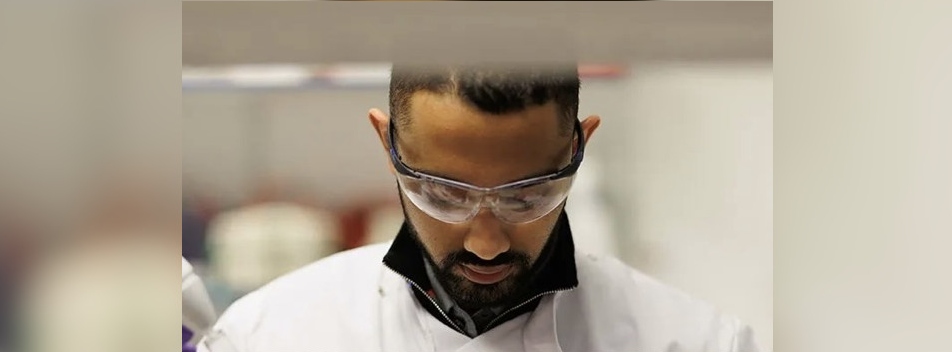 Shakil Khan wearing a lab coat and protective glasses, looking down